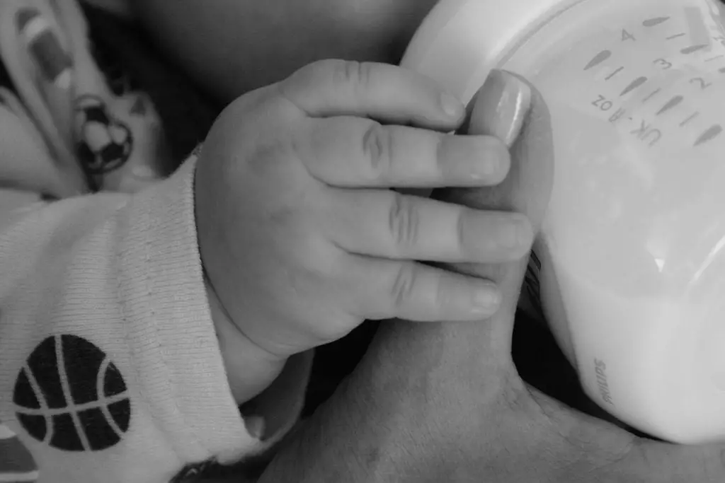 Baby feeding from a bottle holding mom's finger