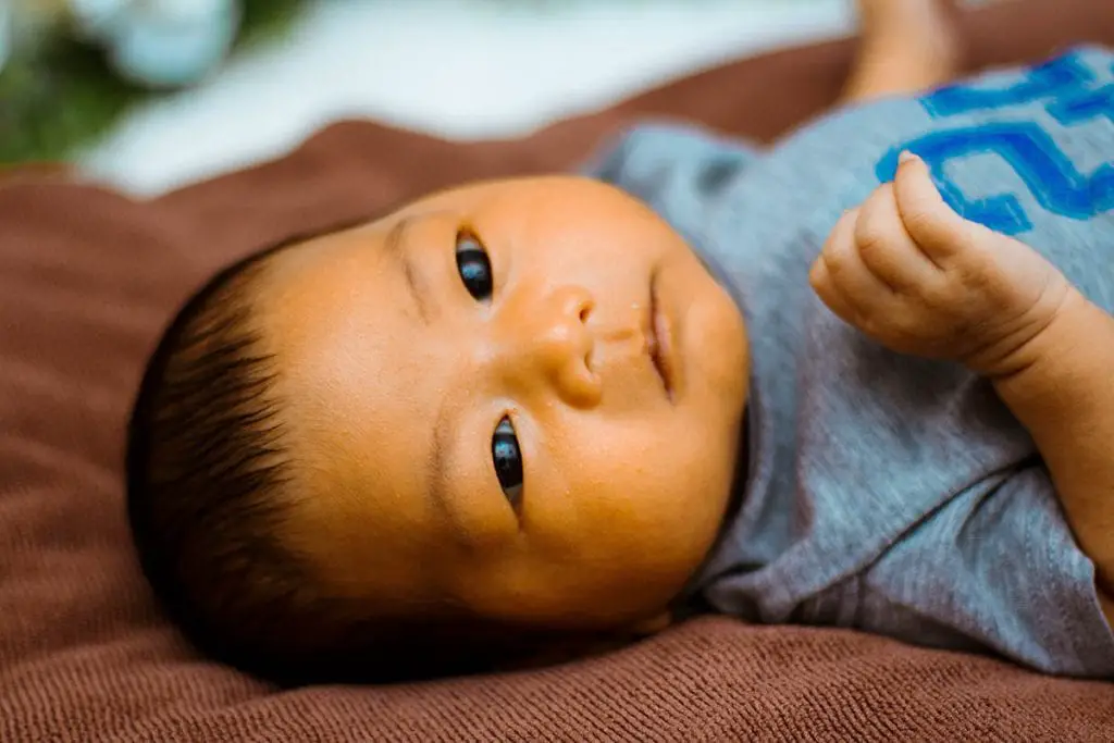 baby in blue shirt lying on brown bed