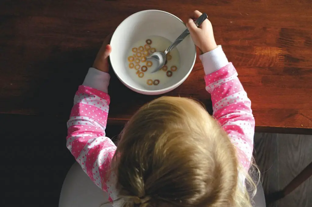 girl eating a cereal in a white bowl